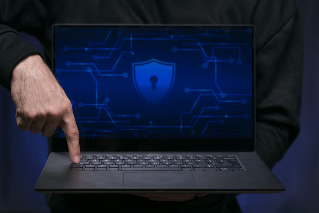 Laptop screen showing digital lock icon with cybersecurity elements like firewall and encryption in a high-tech workspace.